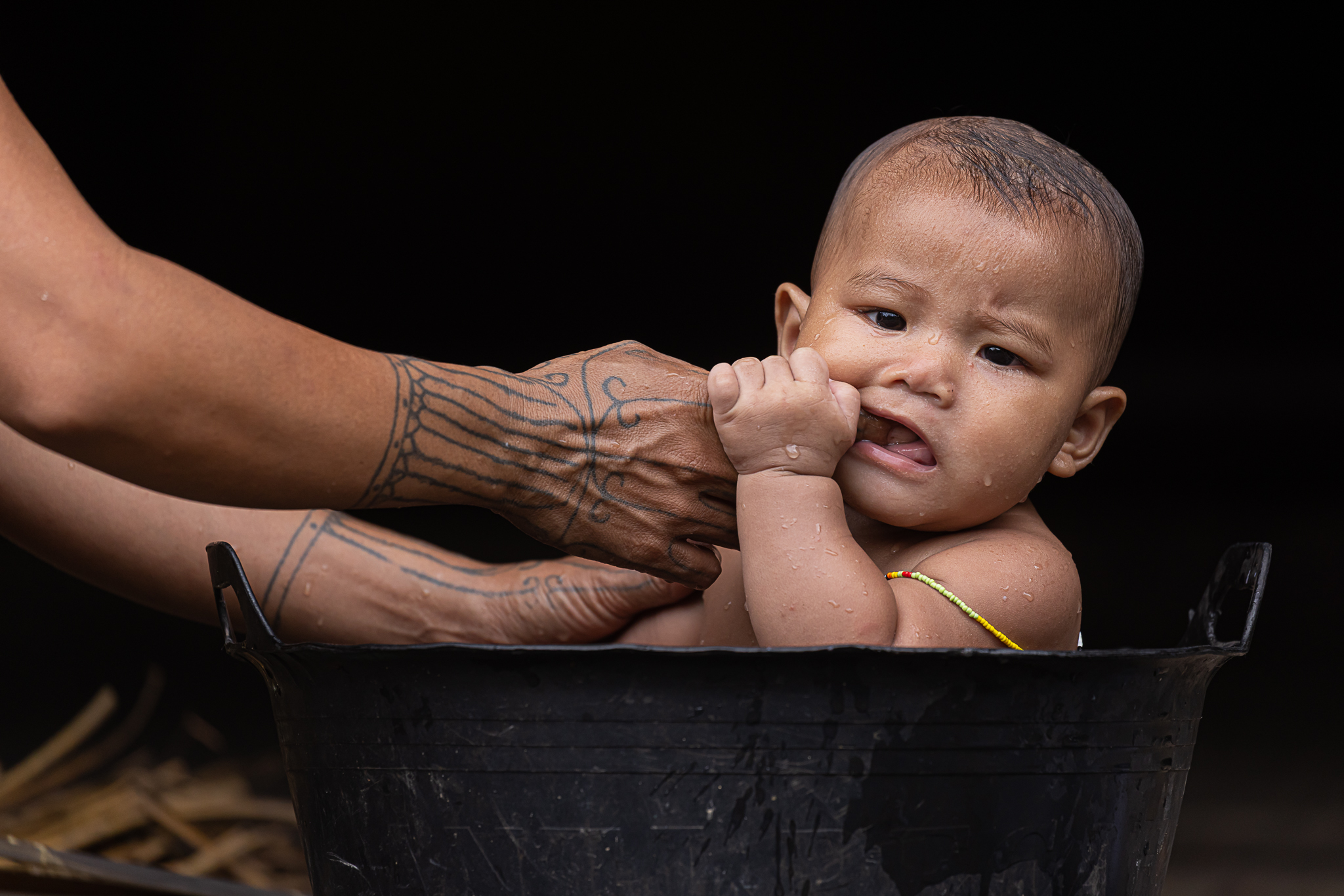 Baby bathing in a black bucket.
